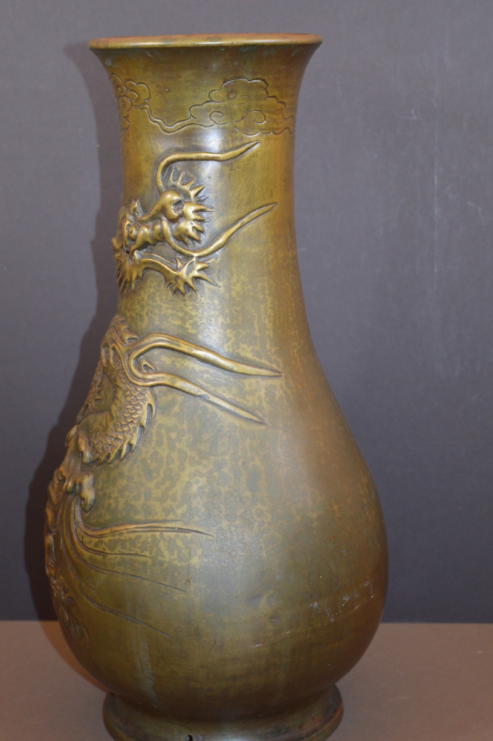 A tall baluster-shaped bronze vase featuring a high-relief carved dragon emerging from swirling waves and cloud motifs. View V