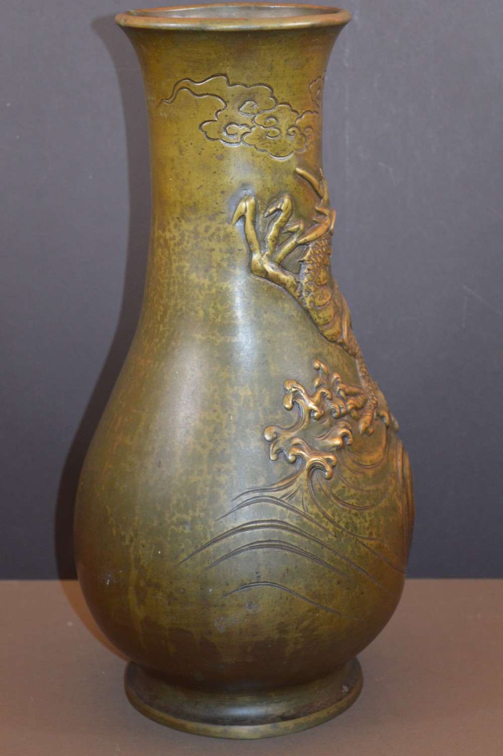 A tall baluster-shaped bronze vase featuring a high-relief carved dragon emerging from swirling waves and cloud motifs. View VII