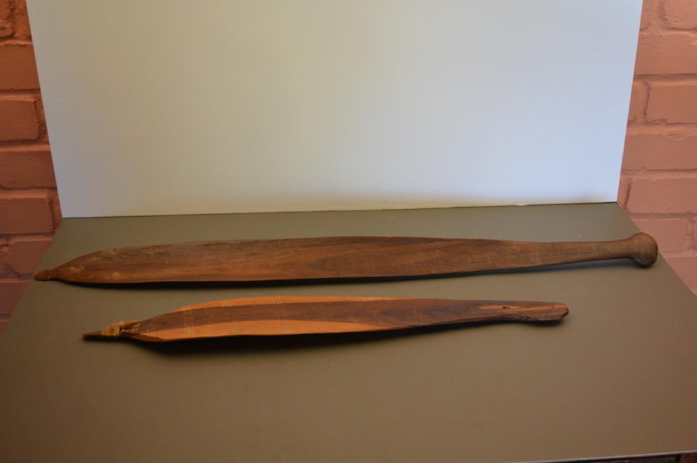 A pair of 19th-century carved Indigenous Australian wooden woomeras displaying elongated curved profiles and natural timber grain.