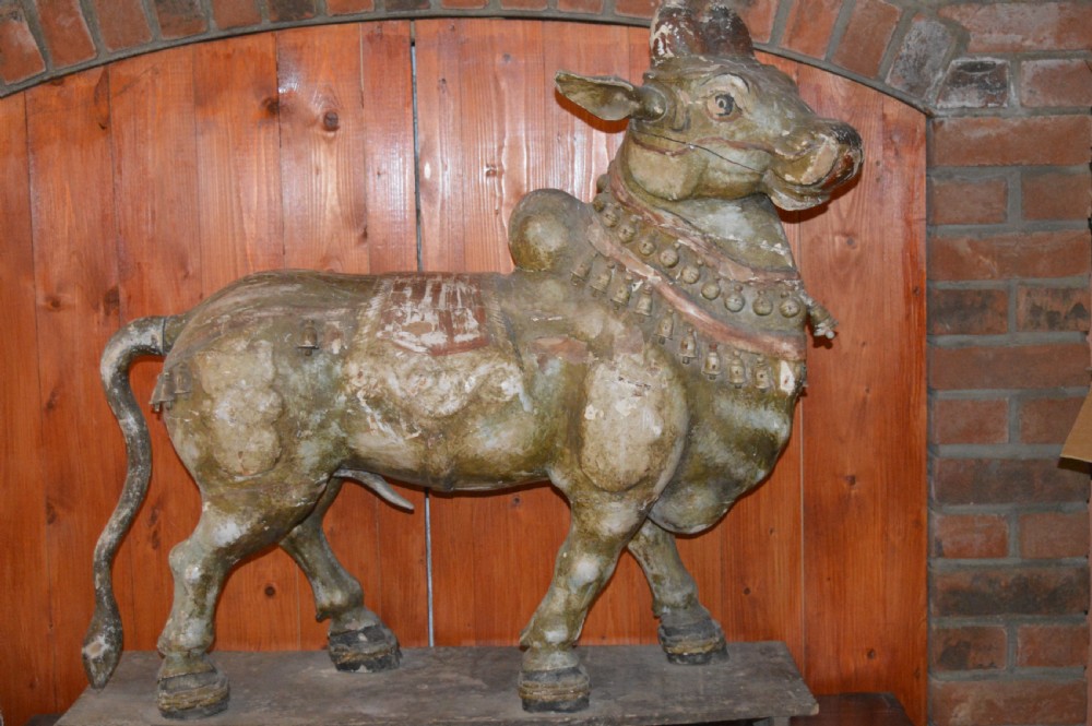 A large antique carved wooden Nandi bull statue featuring worn polychrome paint and decorative carved bells around its neck.