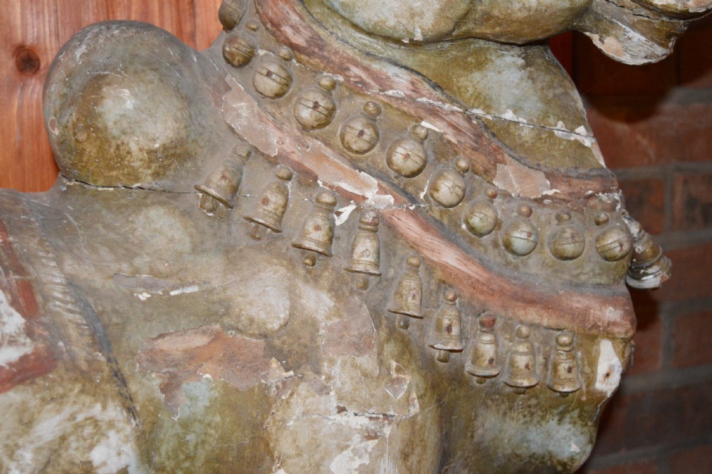 A large antique carved wooden Nandi bull statue featuring worn polychrome paint and decorative carved bells around its neck. View V
