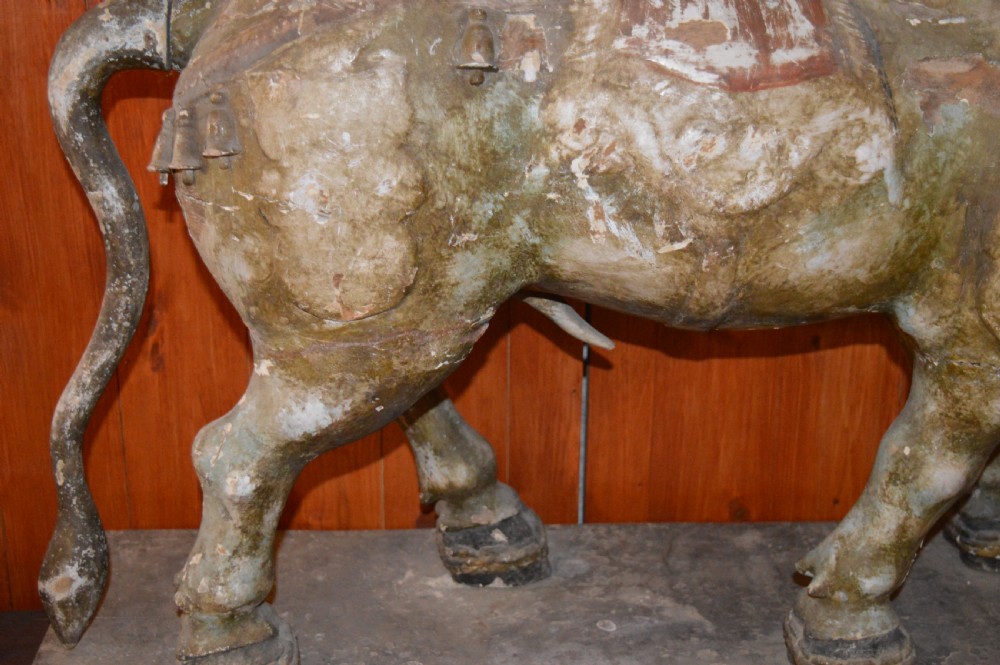 A large antique carved wooden Nandi bull statue featuring worn polychrome paint and decorative carved bells around its neck. View VII