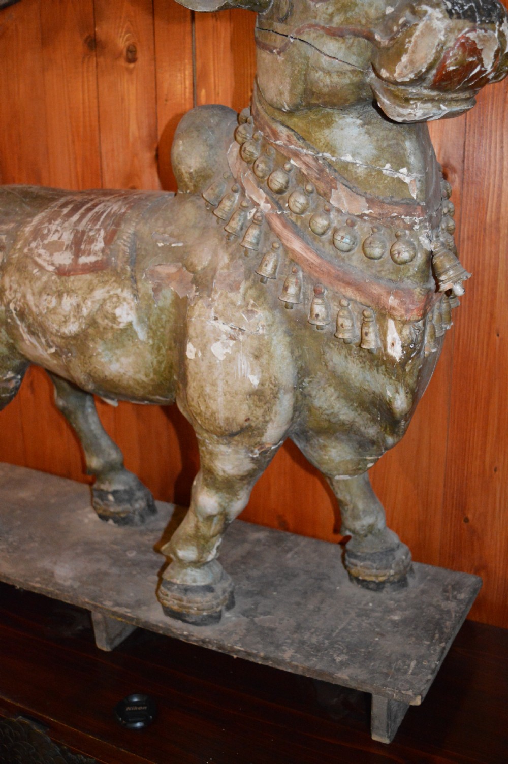 A large antique carved wooden Nandi bull statue featuring worn polychrome paint and decorative carved bells around its neck. View XIII