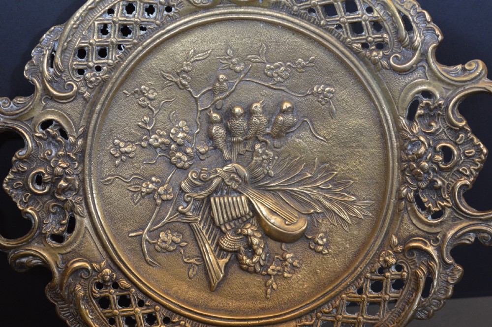 A cast bronze decorative centrepiece plate featuring a high-relief central scene with birds and musical instruments surrounded by an openwork lattice border and scroll handles. View VIII
