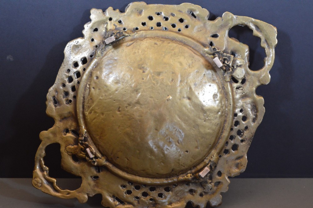 A cast bronze decorative centrepiece plate featuring a high-relief central scene with birds and musical instruments surrounded by an openwork lattice border and scroll handles. View IX