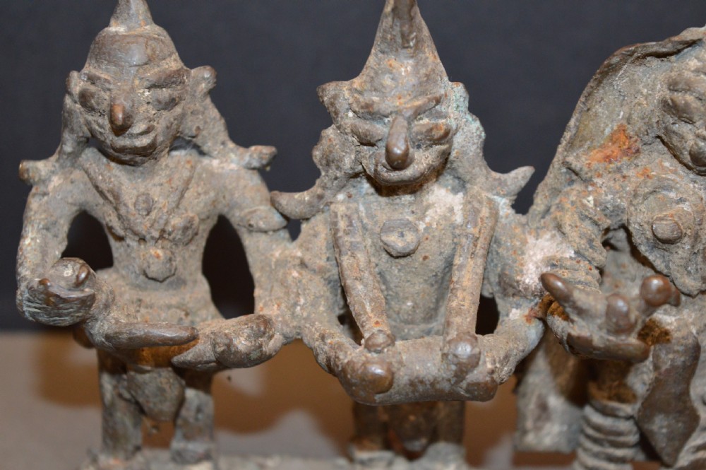 An antique dark bronze Indian sculpture featuring three standing Hindu deities with conical headwear on a shared rectangular base. View III