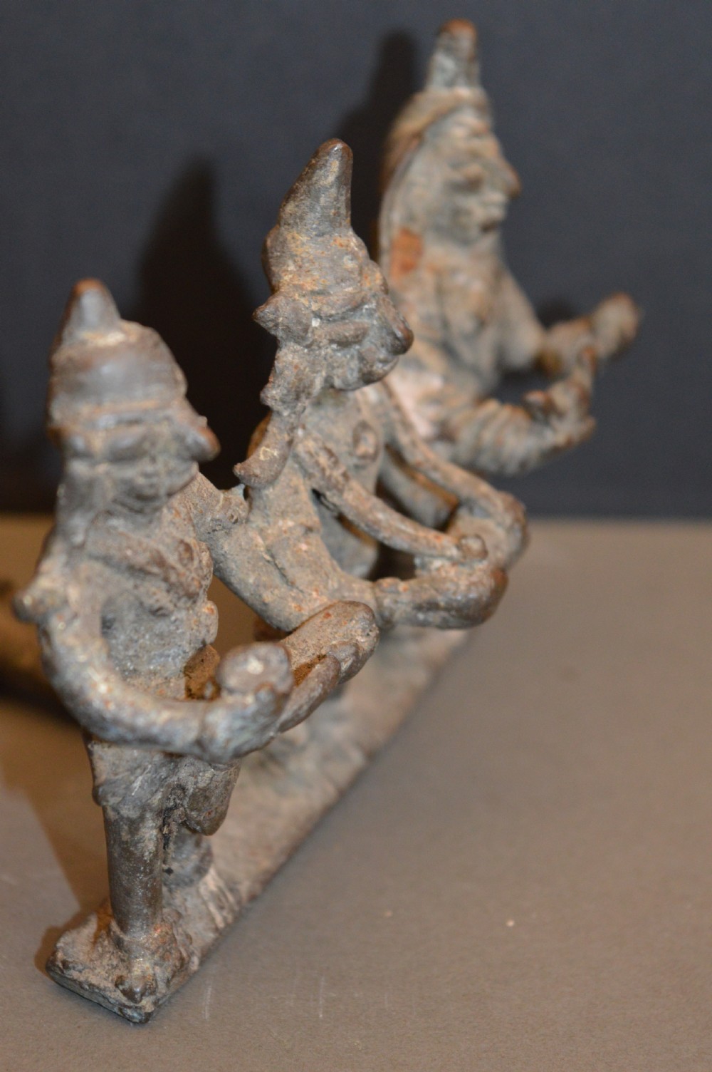 An antique dark bronze Indian sculpture featuring three standing Hindu deities with conical headwear on a shared rectangular base. View VII