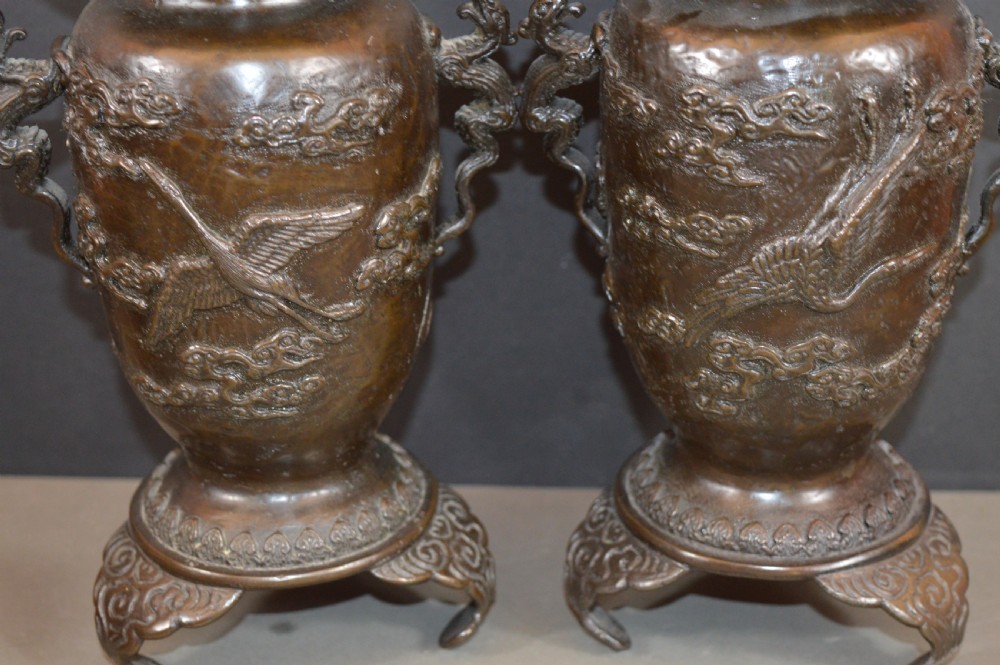 A pair of dark bronze Meiji period Japanese vases with high-relief figural decoration, dragon handles, and tripod bases. View X