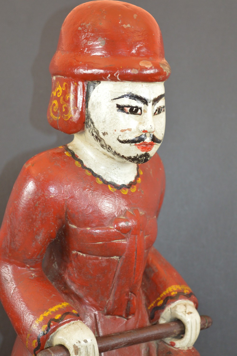 A late nineteenth-century carved wooden Tibetan figure painted in red, green, and white polychrome, depicting a standing male figure holding a rod above a serpent motif. View II