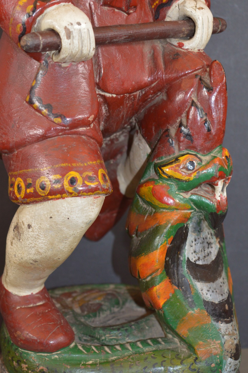 A late nineteenth-century carved wooden Tibetan figure painted in red, green, and white polychrome, depicting a standing male figure holding a rod above a serpent motif. View III