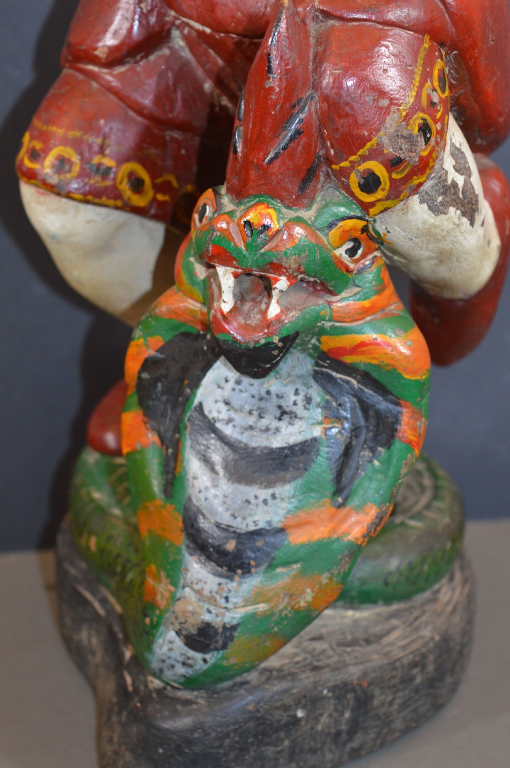 A late nineteenth-century carved wooden Tibetan figure painted in red, green, and white polychrome, depicting a standing male figure holding a rod above a serpent motif. View IV