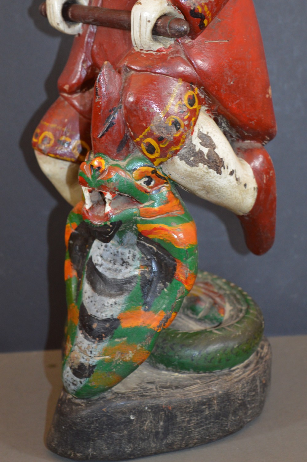 A late nineteenth-century carved wooden Tibetan figure painted in red, green, and white polychrome, depicting a standing male figure holding a rod above a serpent motif. View VI