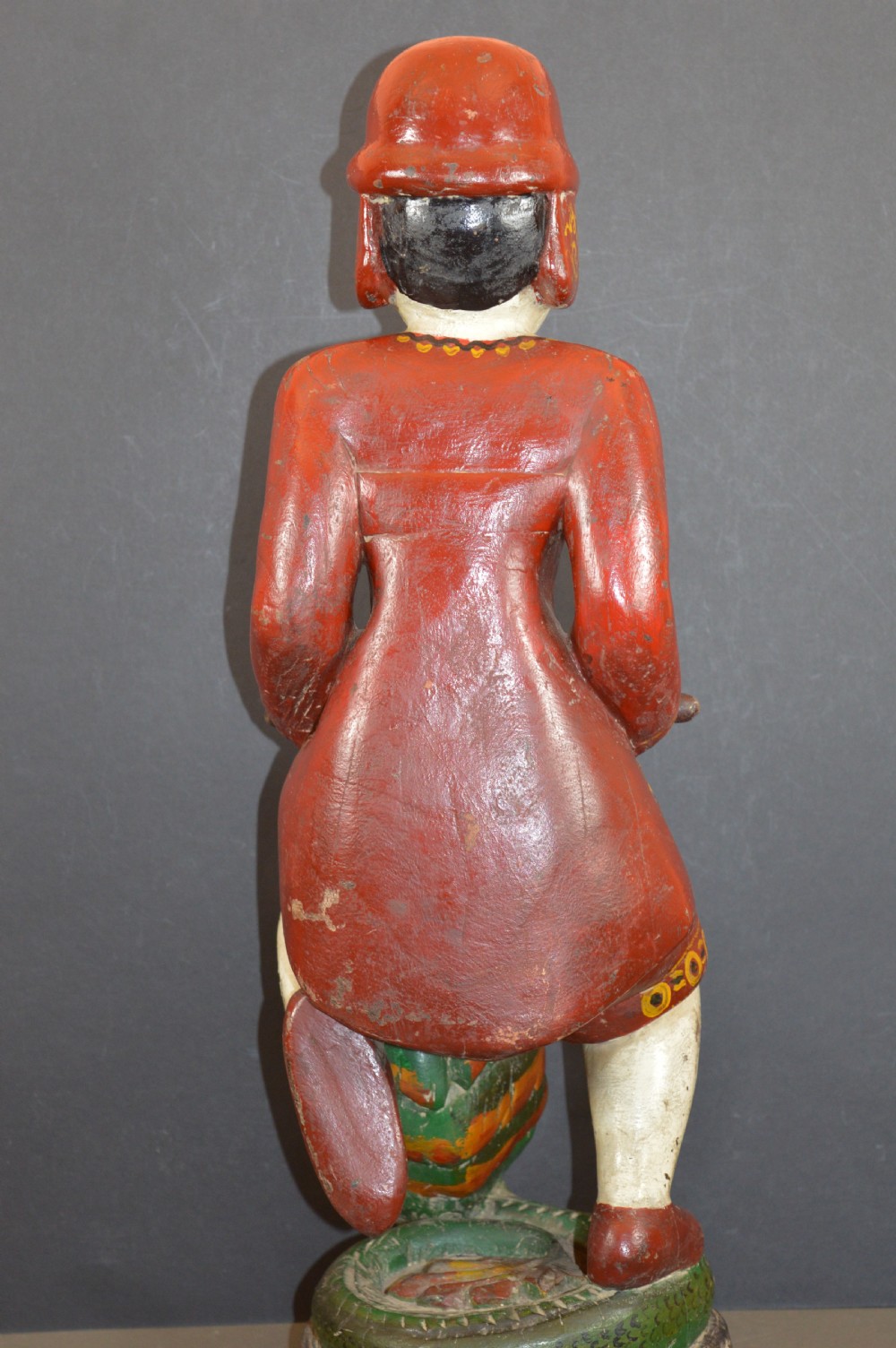 A late nineteenth-century carved wooden Tibetan figure painted in red, green, and white polychrome, depicting a standing male figure holding a rod above a serpent motif. View VII