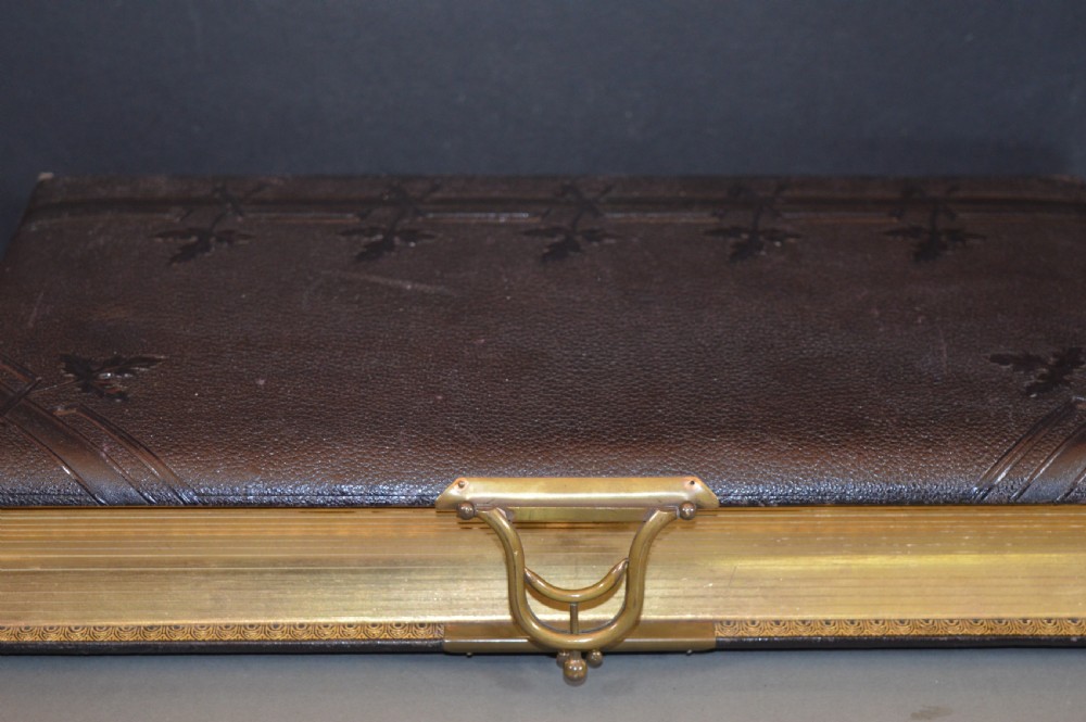 A dark brown Victorian leather photo album featuring embossed leaf motifs along the spine and a brass clasp on the edge. View IV