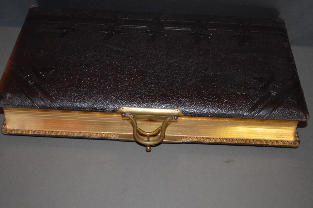 A dark brown Victorian leather photo album featuring embossed leaf motifs along the spine and a brass clasp on the edge. View V