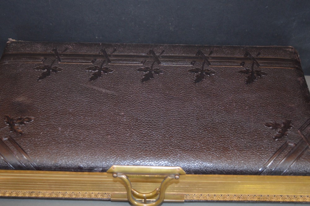 A dark brown Victorian leather photo album featuring embossed leaf motifs along the spine and a brass clasp on the edge. View VI