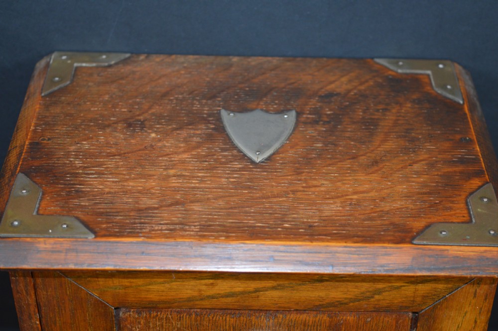 A late 19th-century oak desktop smokers cabinet featuring brass corner mounts and a central relief carving of an Indian deity. View III
