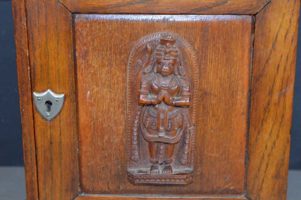 A late 19th-century oak desktop smokers cabinet featuring brass corner mounts and a central relief carving of an Indian deity. View IV