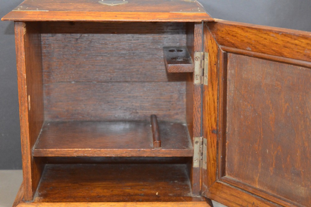 A late 19th-century oak desktop smokers cabinet featuring brass corner mounts and a central relief carving of an Indian deity. View V