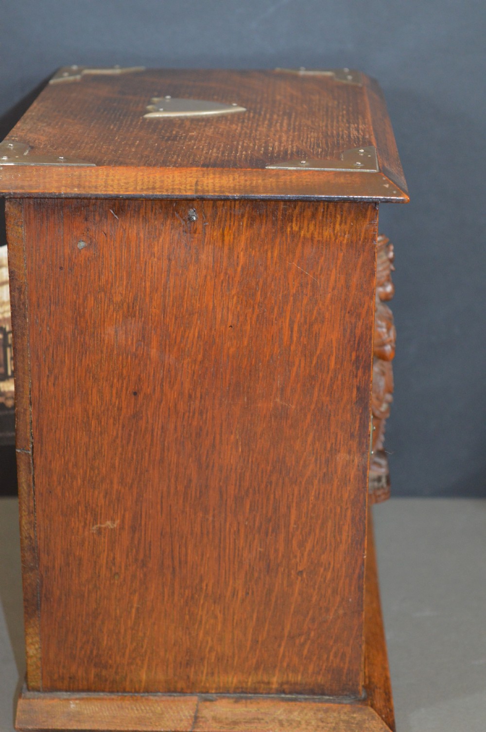 A late 19th-century oak desktop smokers cabinet featuring brass corner mounts and a central relief carving of an Indian deity. View VI