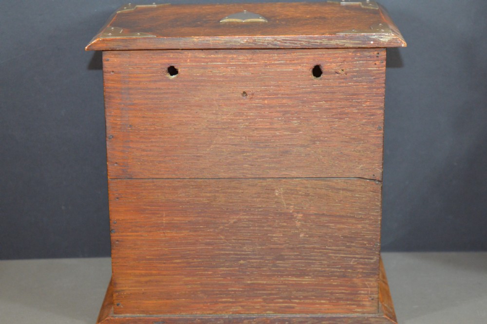 A late 19th-century oak desktop smokers cabinet featuring brass corner mounts and a central relief carving of an Indian deity. View VII