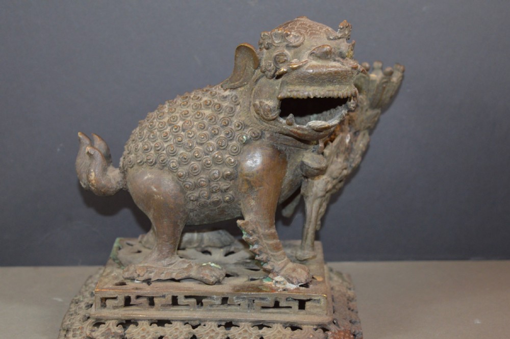 A late 18th-century Chinese bronze incense burner in the shape of a mythical Qilin creature with an open mouth standing on a pierced rectangular stand.