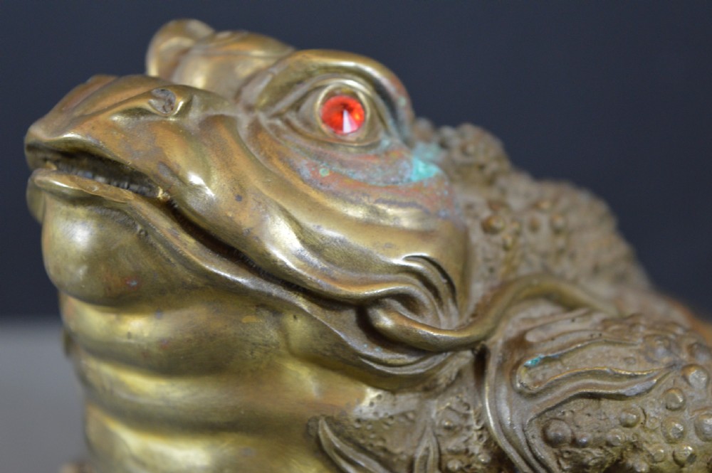 A heavy cast bronze three-legged money toad sculpture with red glass eyes, sitting on a base of Chinese coins and ingots. View II