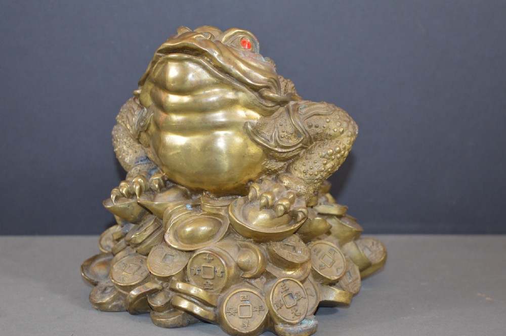 A heavy cast bronze three-legged money toad sculpture with red glass eyes, sitting on a base of Chinese coins and ingots. View III