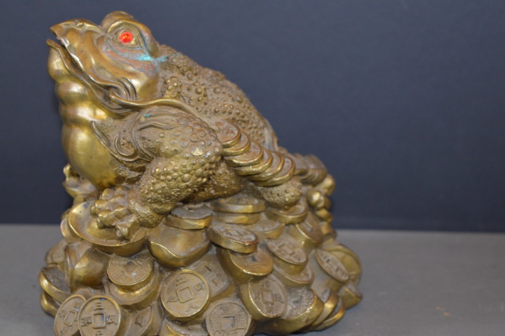 A heavy cast bronze three-legged money toad sculpture with red glass eyes, sitting on a base of Chinese coins and ingots. View IV