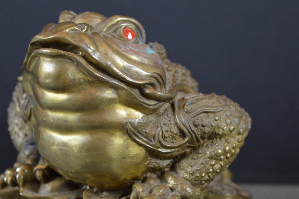 A heavy cast bronze three-legged money toad sculpture with red glass eyes, sitting on a base of Chinese coins and ingots. View V