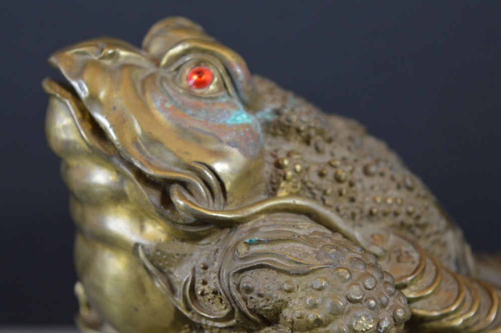 A heavy cast bronze three-legged money toad sculpture with red glass eyes, sitting on a base of Chinese coins and ingots. View VI