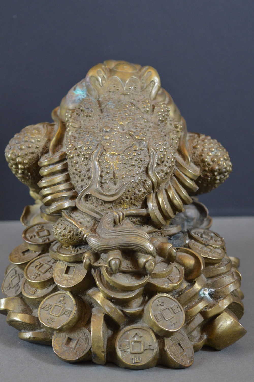 A heavy cast bronze three-legged money toad sculpture with red glass eyes, sitting on a base of Chinese coins and ingots. View VII