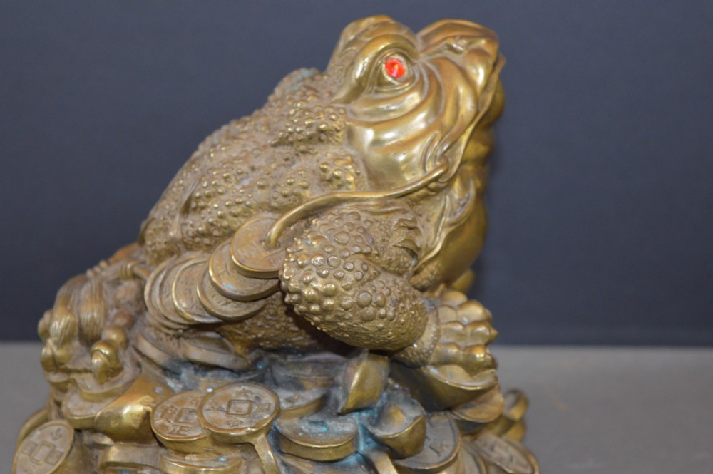 A heavy cast bronze three-legged money toad sculpture with red glass eyes, sitting on a base of Chinese coins and ingots. View VIII
