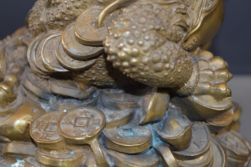 A heavy cast bronze three-legged money toad sculpture with red glass eyes, sitting on a base of Chinese coins and ingots. View IX