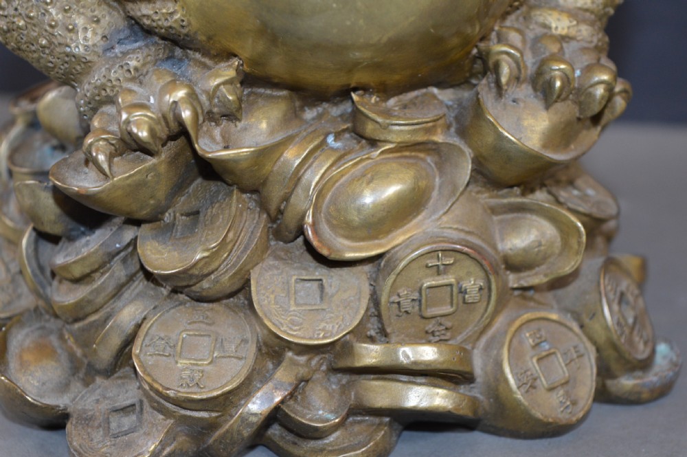 A heavy cast bronze three-legged money toad sculpture with red glass eyes, sitting on a base of Chinese coins and ingots. View X