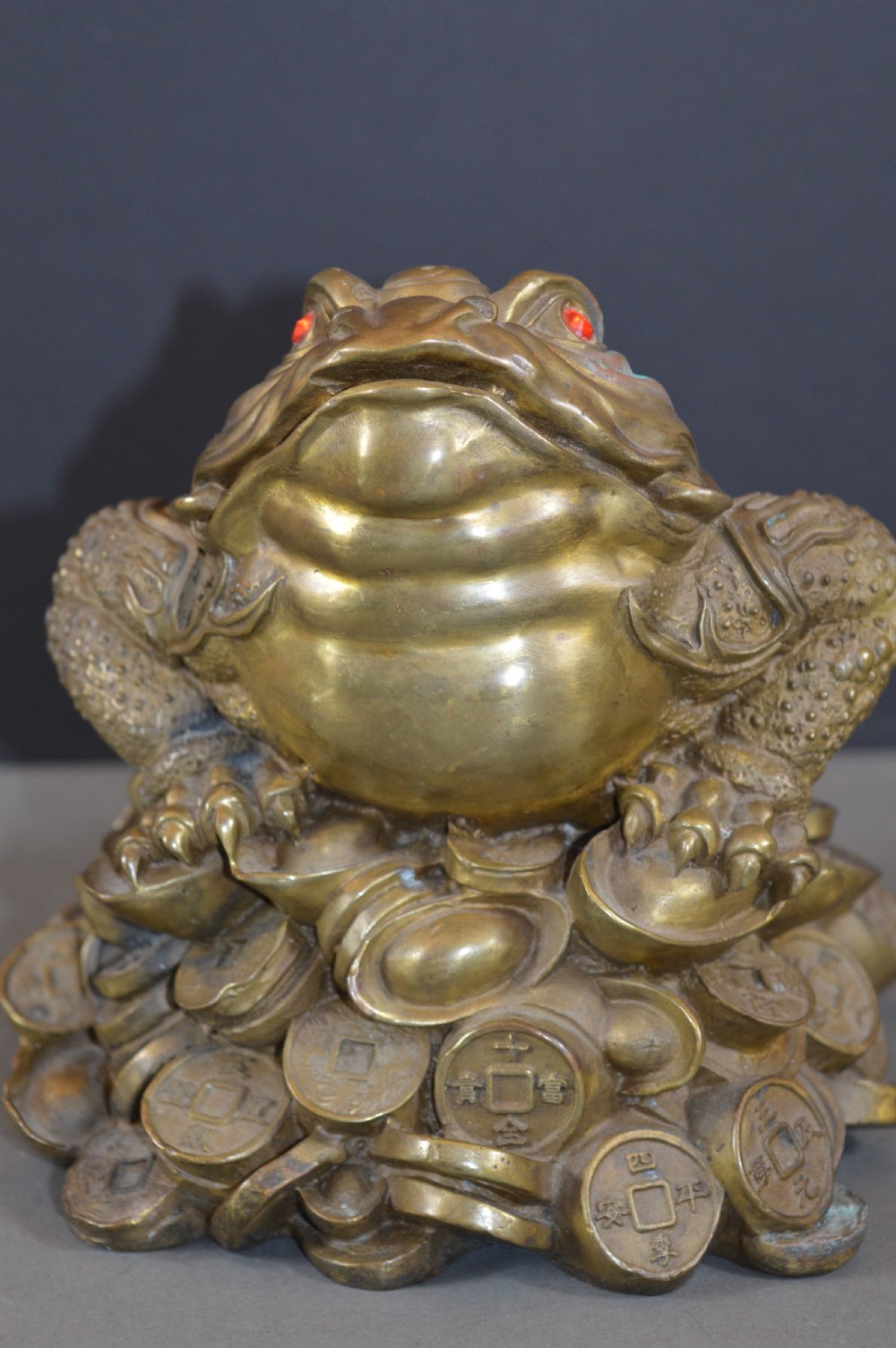 A heavy cast bronze three-legged money toad sculpture with red glass eyes, sitting on a base of Chinese coins and ingots. View XII