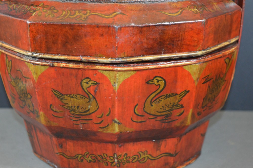 A red hand-painted Chinese wooden rice carrier featuring an arched overhead handle, lidded faceted body, and depictions of waterbirds and fish. View II