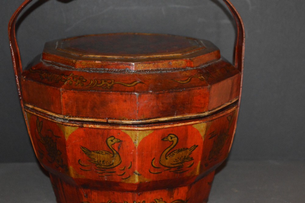 A red hand-painted Chinese wooden rice carrier featuring an arched overhead handle, lidded faceted body, and depictions of waterbirds and fish. View III