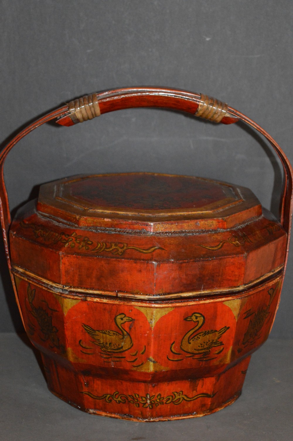 A red hand-painted Chinese wooden rice carrier featuring an arched overhead handle, lidded faceted body, and depictions of waterbirds and fish. View IV
