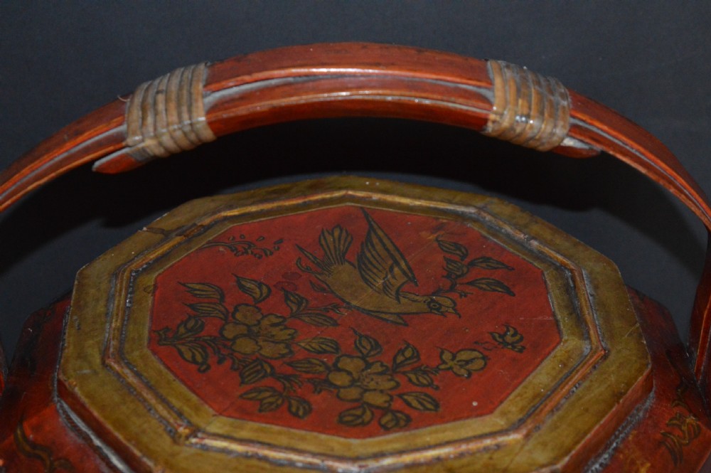 A red hand-painted Chinese wooden rice carrier featuring an arched overhead handle, lidded faceted body, and depictions of waterbirds and fish. View V