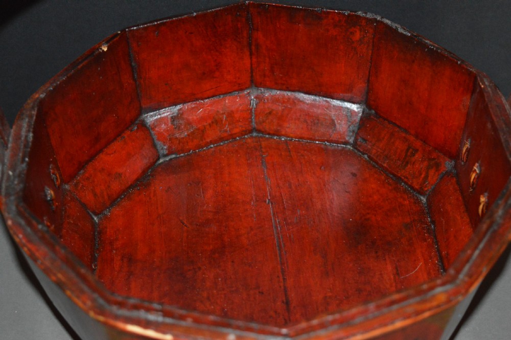 A red hand-painted Chinese wooden rice carrier featuring an arched overhead handle, lidded faceted body, and depictions of waterbirds and fish. View X
