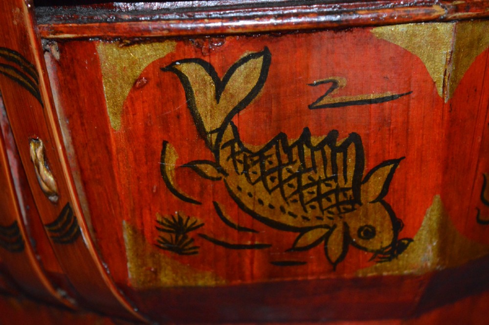 A red hand-painted Chinese wooden rice carrier featuring an arched overhead handle, lidded faceted body, and depictions of waterbirds and fish. View XII