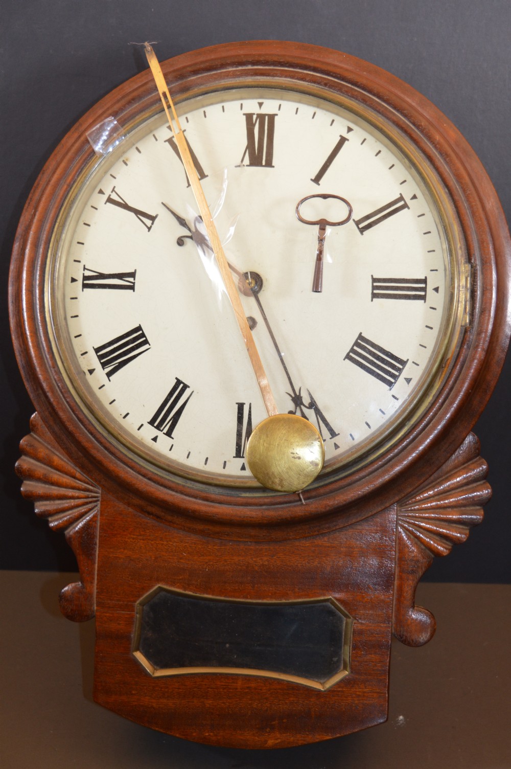 A Victorian mahogany drop dial fusee wall clock featuring a white circular dial with Roman numerals, carved side ears, and a lower pendulum window. View VIII