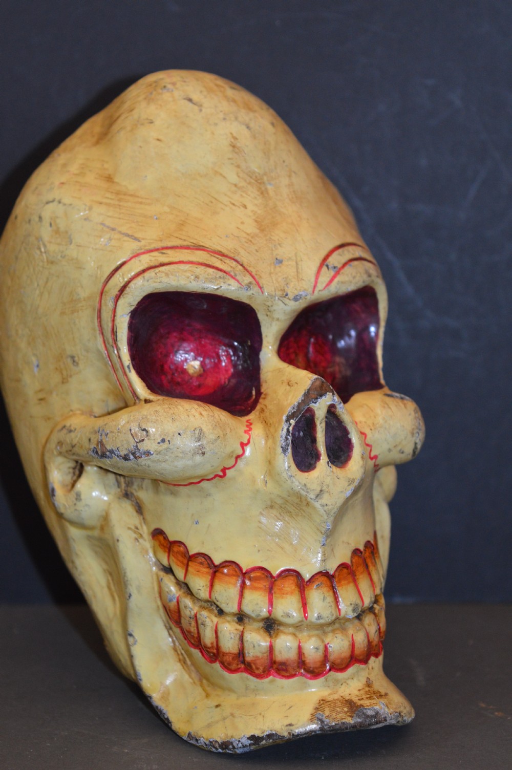 A hand-carved and painted yellow wooden Tibetan Citipati skull featuring deep red eye sockets and sculpted teeth.