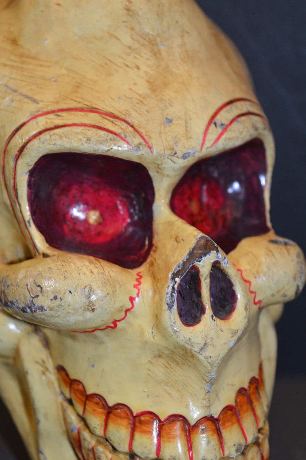 A hand-carved and painted yellow wooden Tibetan Citipati skull featuring deep red eye sockets and sculpted teeth. View II