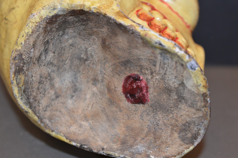 A hand-carved and painted yellow wooden Tibetan Citipati skull featuring deep red eye sockets and sculpted teeth. View III