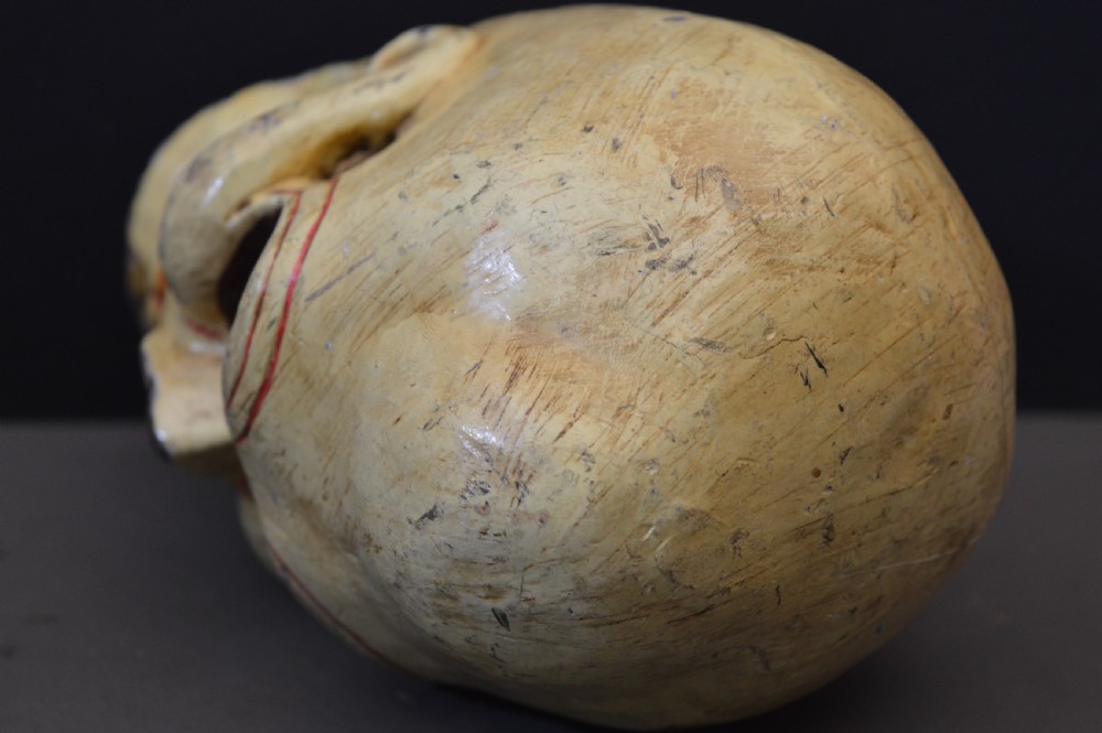 A hand-carved and painted yellow wooden Tibetan Citipati skull featuring deep red eye sockets and sculpted teeth. View V