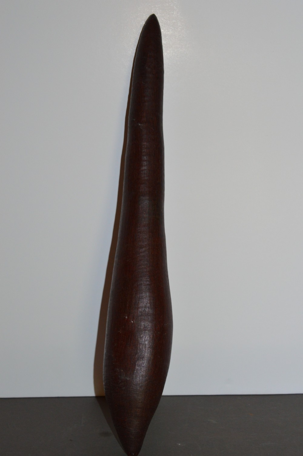 A hand-carved dark hardwood Aboriginal throwing club tapering at both ends with a smooth patinated surface.