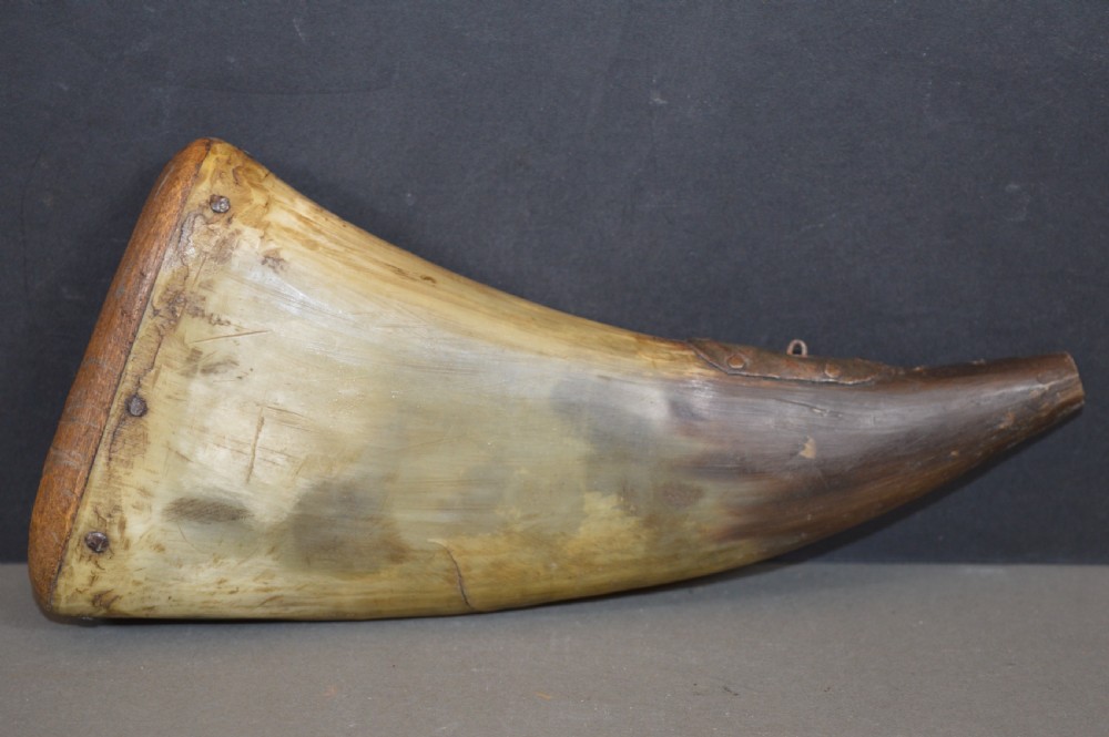 An 18th-century natural curved horn powder flask featuring a fitted wooden base plug pinned with iron tacks and a tapered spout.