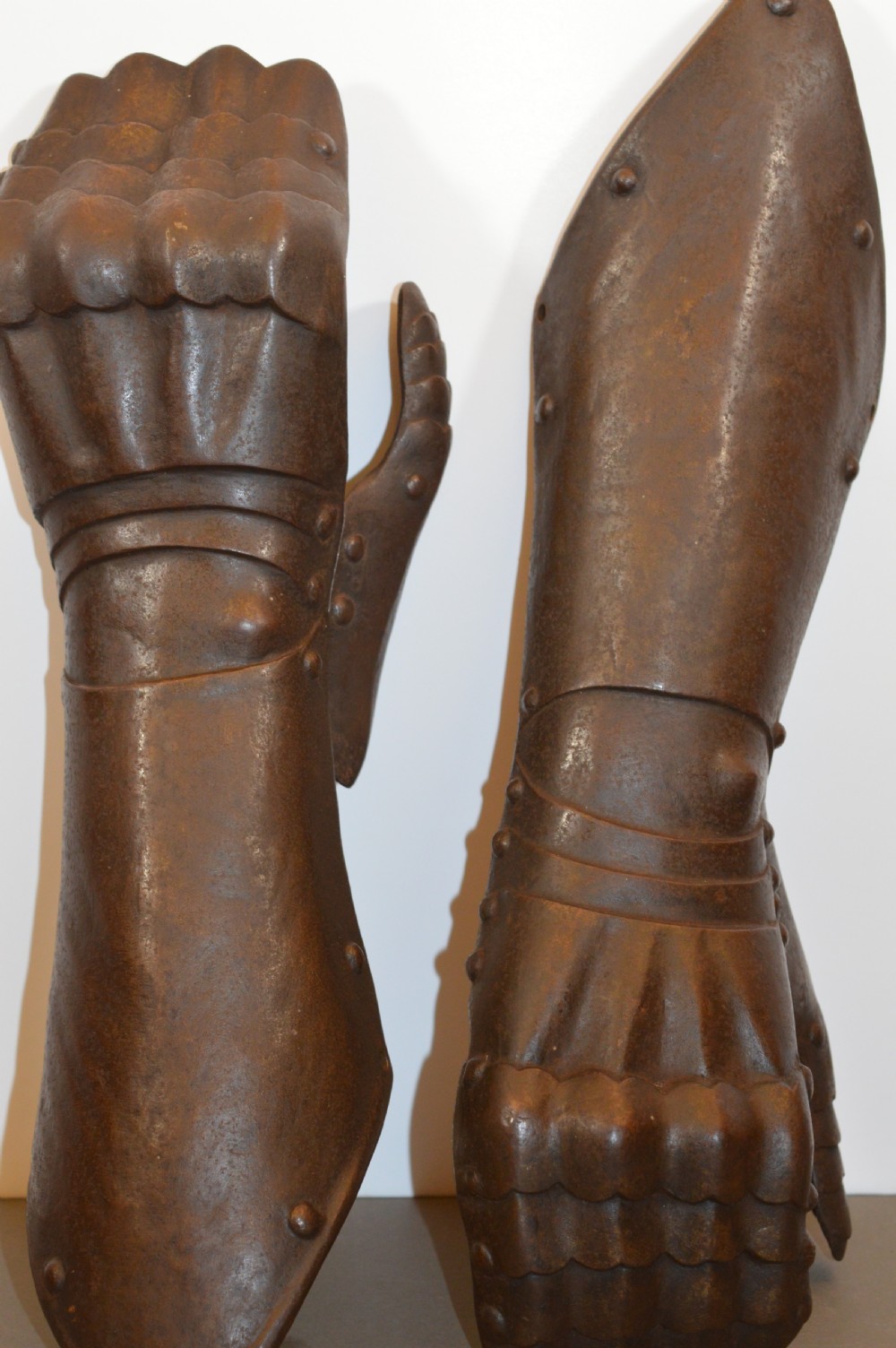 A pair of 19th-century articulated iron armour gauntlets with layered finger plates, flared cuffs, and visible rivets with an oxidised patina.